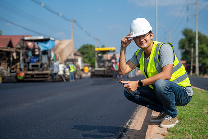 Man in hardhat kneeling by new asphalt
