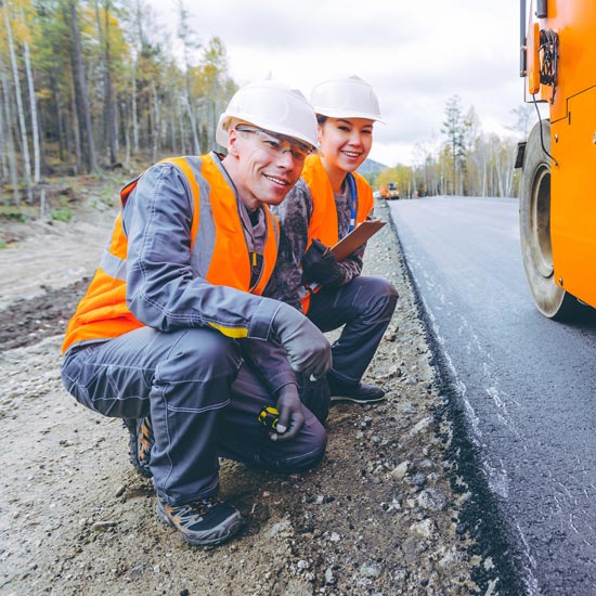 Two workers in PPE kneeling by roadwork